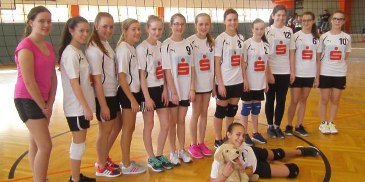 Mädchenmannschaft posiert vor Volleyballnetz